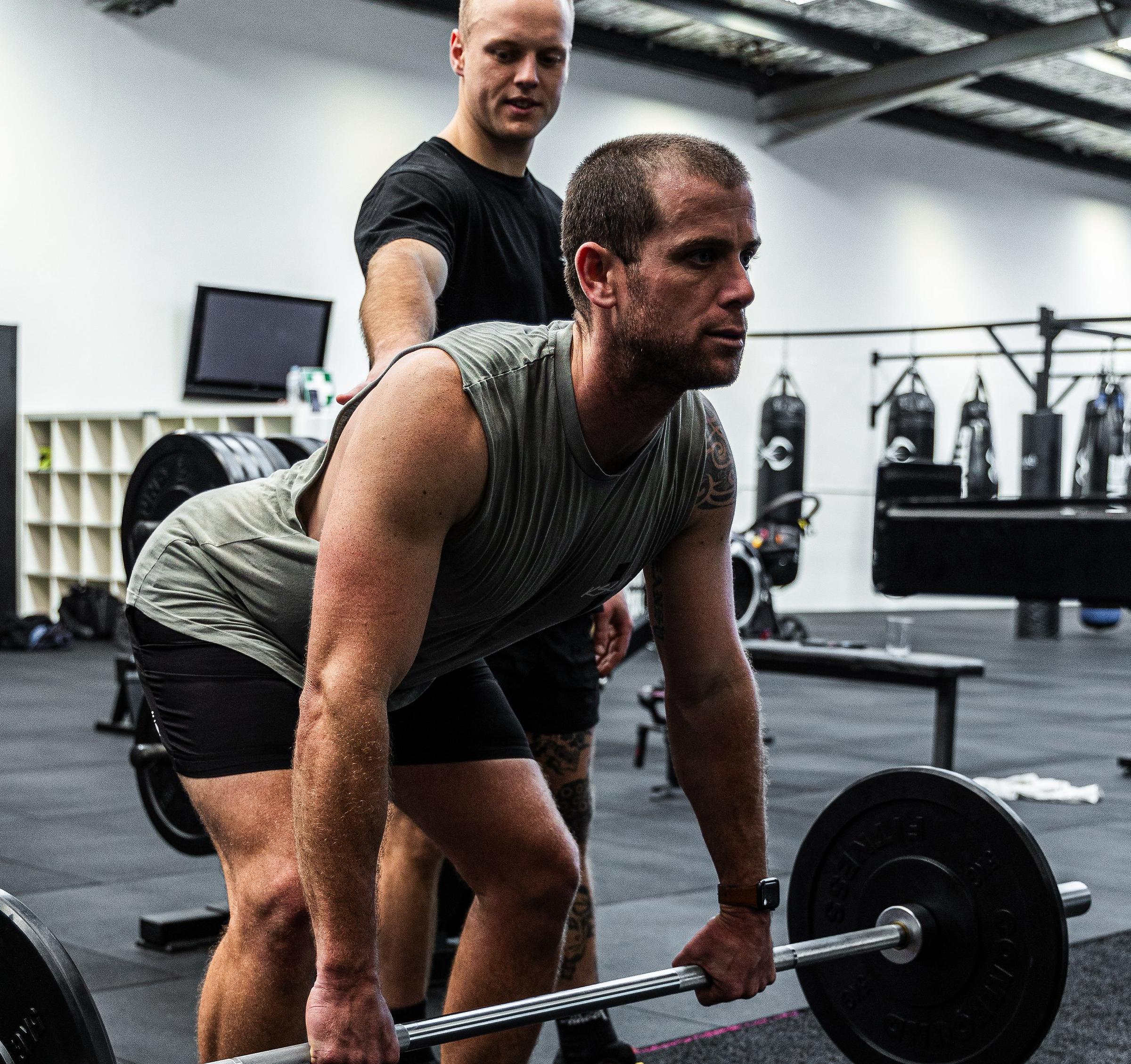 A coach watching a member's deadlift on the strength floor