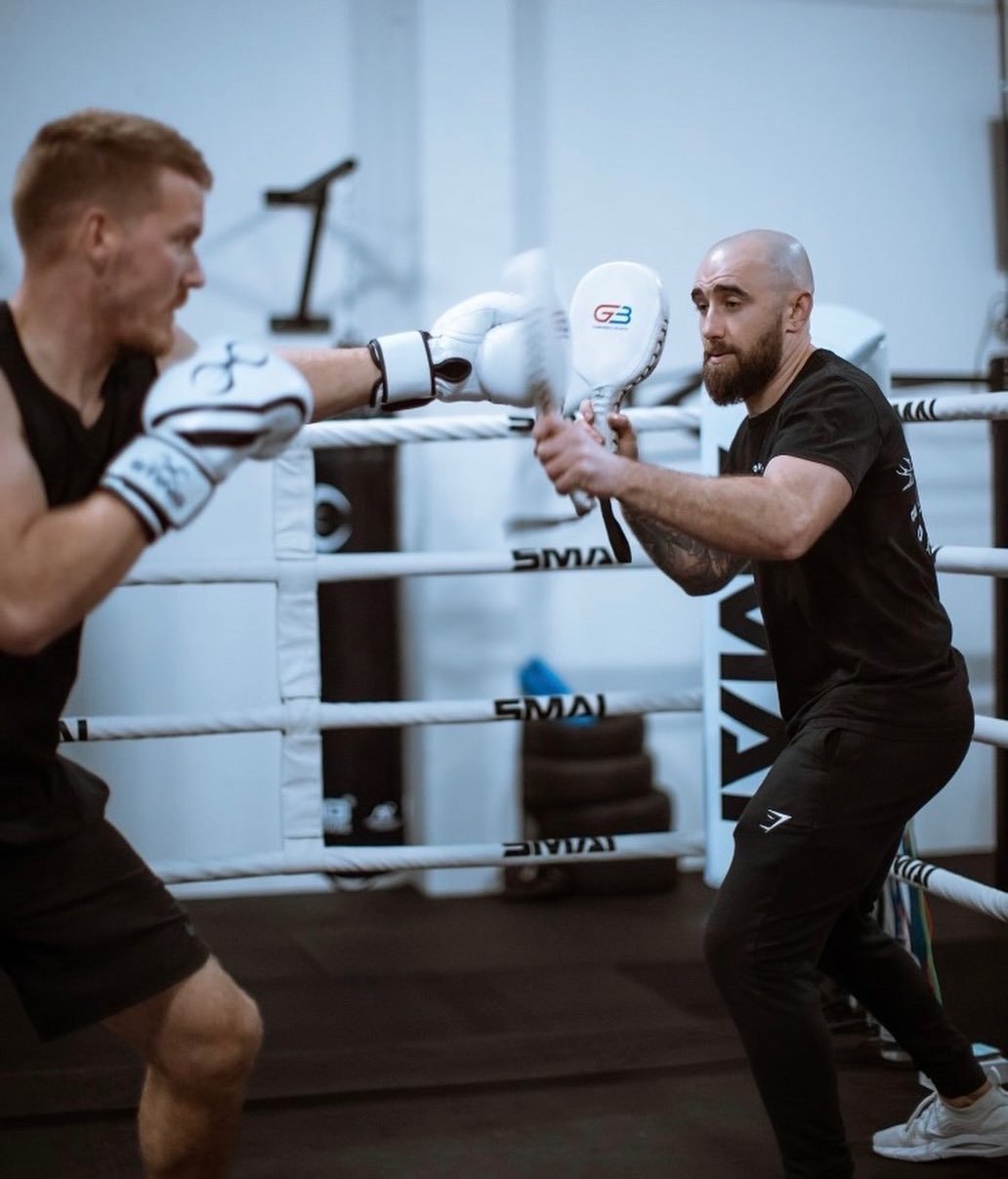 A coach holding pads for a member in front of the ring